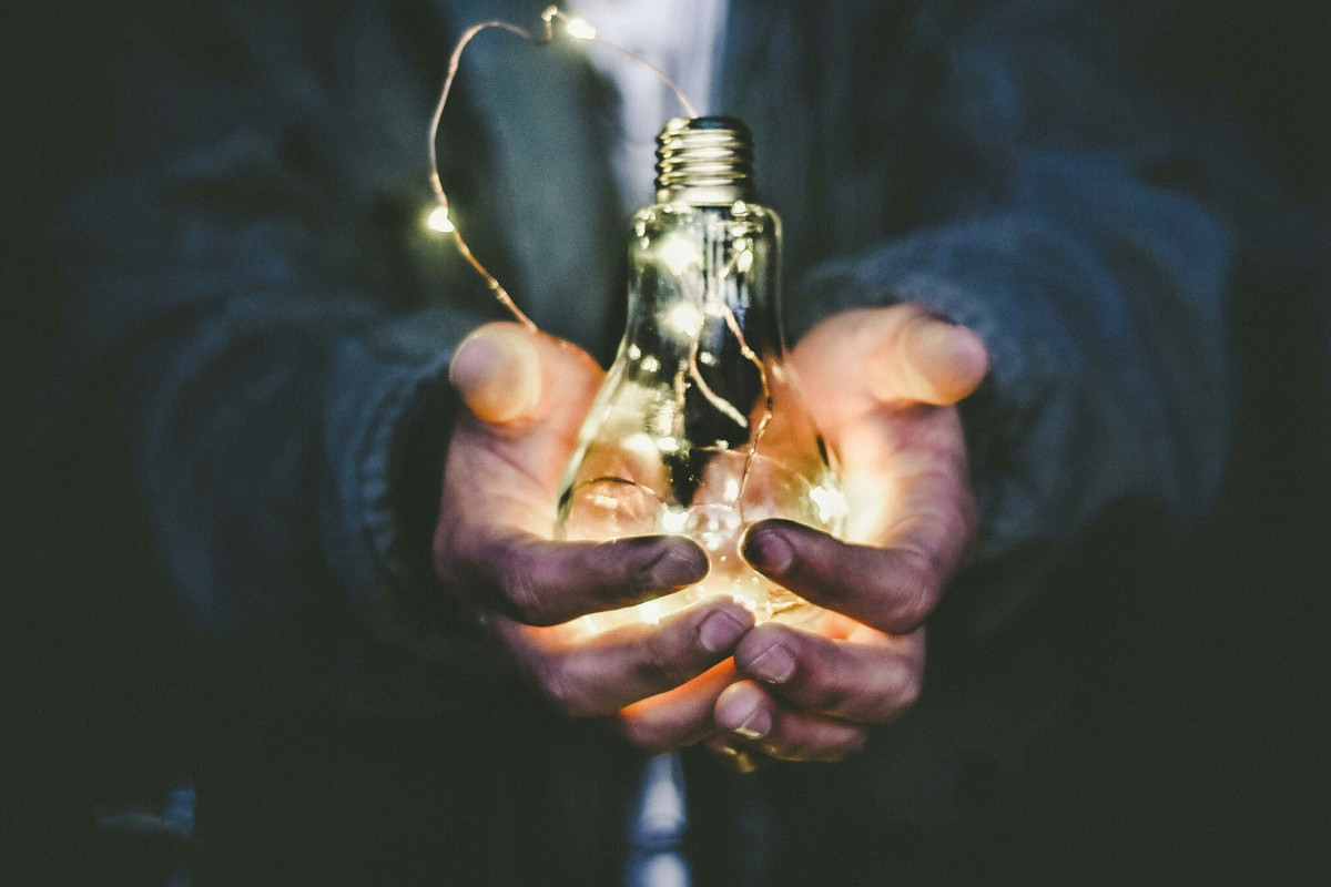 dirty hands holding an illuminated tungstan light bulb with code over it